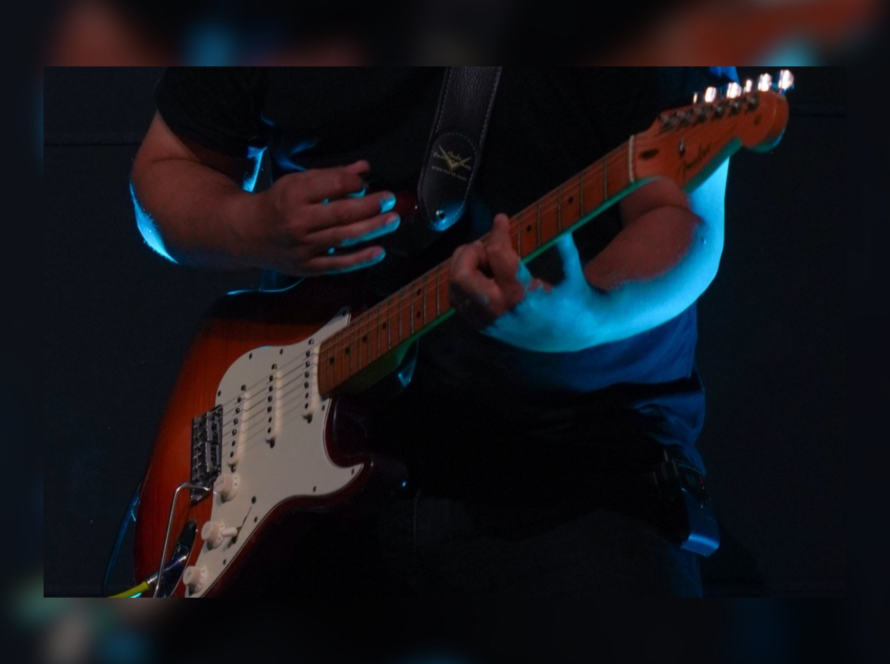 Guitarrista tocando guitarra eléctrica bajo iluminación azul en escenario
